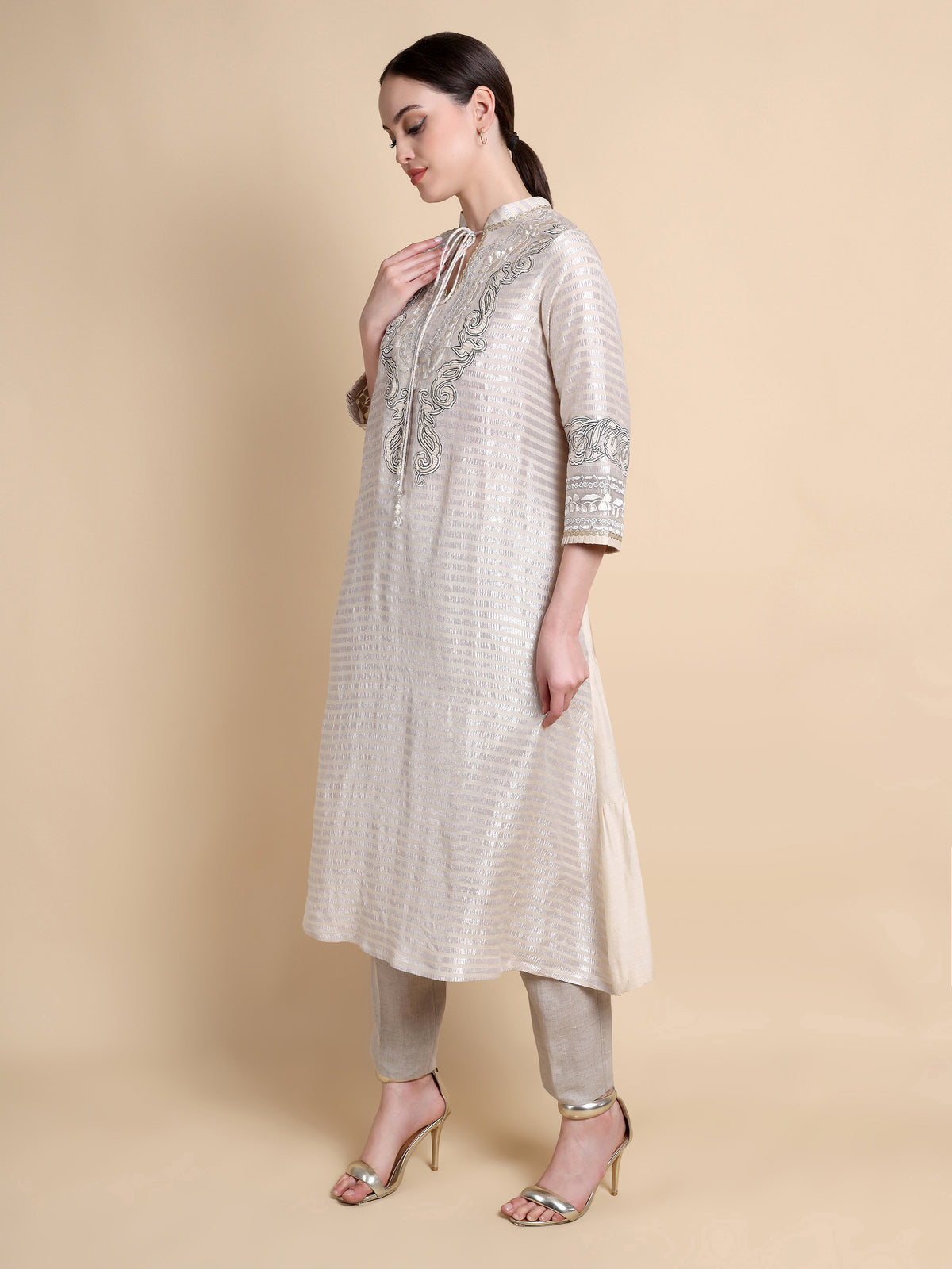 Woman wearing a beige kurta with intricate patterns on a beige background