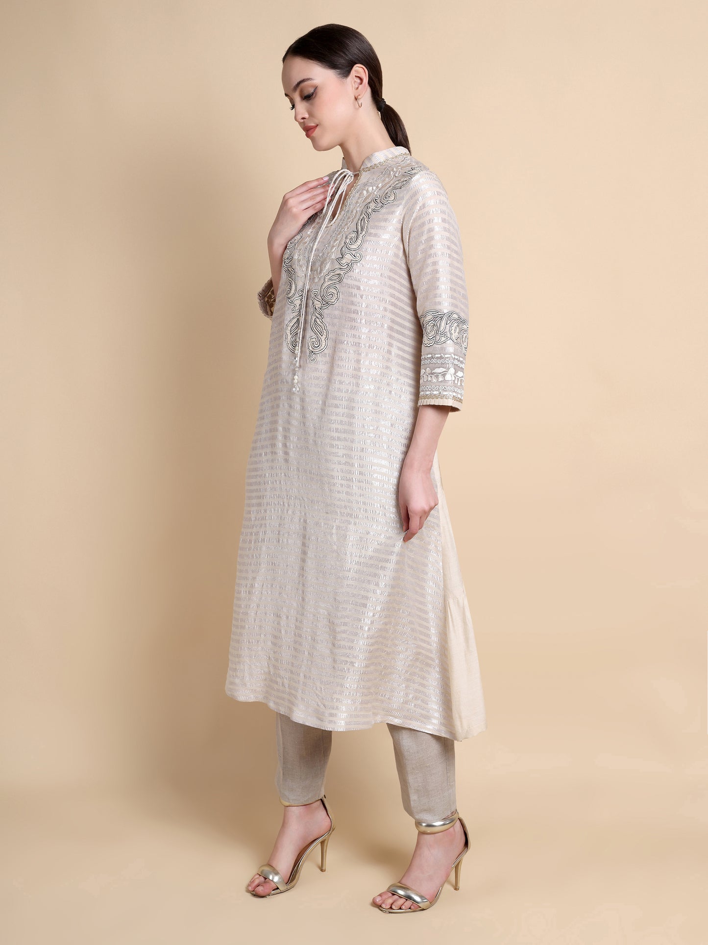 Woman wearing a beige kurta with intricate patterns on a beige background