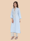 Woman wearing a light blue embroidered kurta with white pants on a beige background