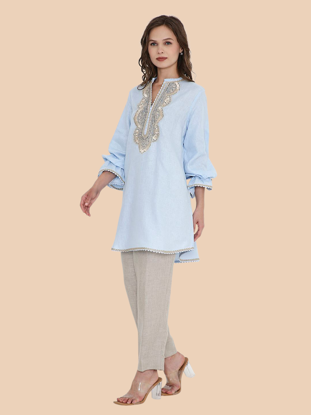 Woman wearing a light blue embroidered top and beige pants on a beige background