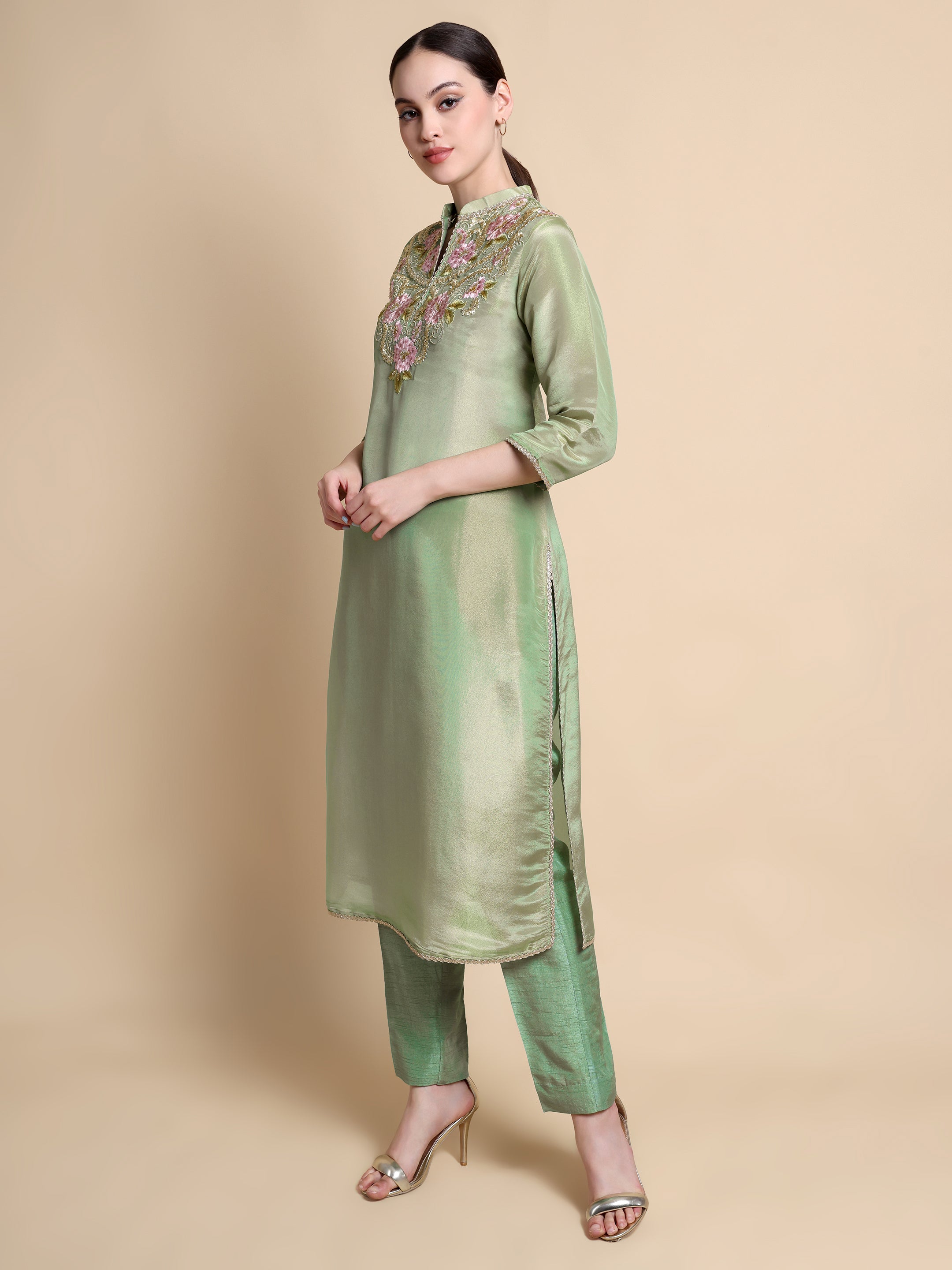 Woman wearing a green kurta with floral embroidery on a beige background