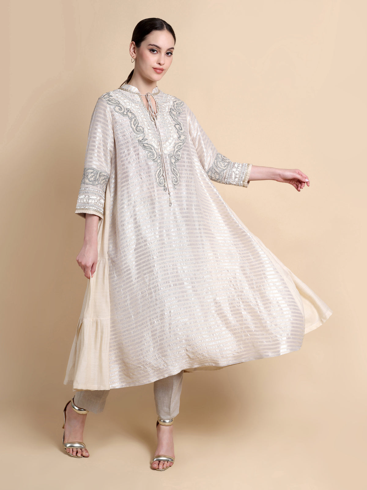 Woman wearing a cream-colored embroidered traditional outfit on a beige background