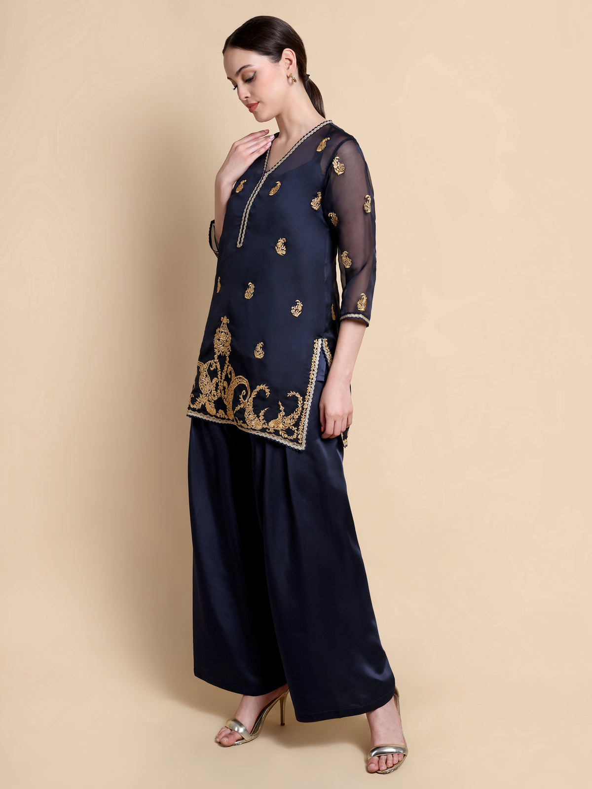 Woman wearing a navy blue traditional outfit with gold embroidery on a beige background