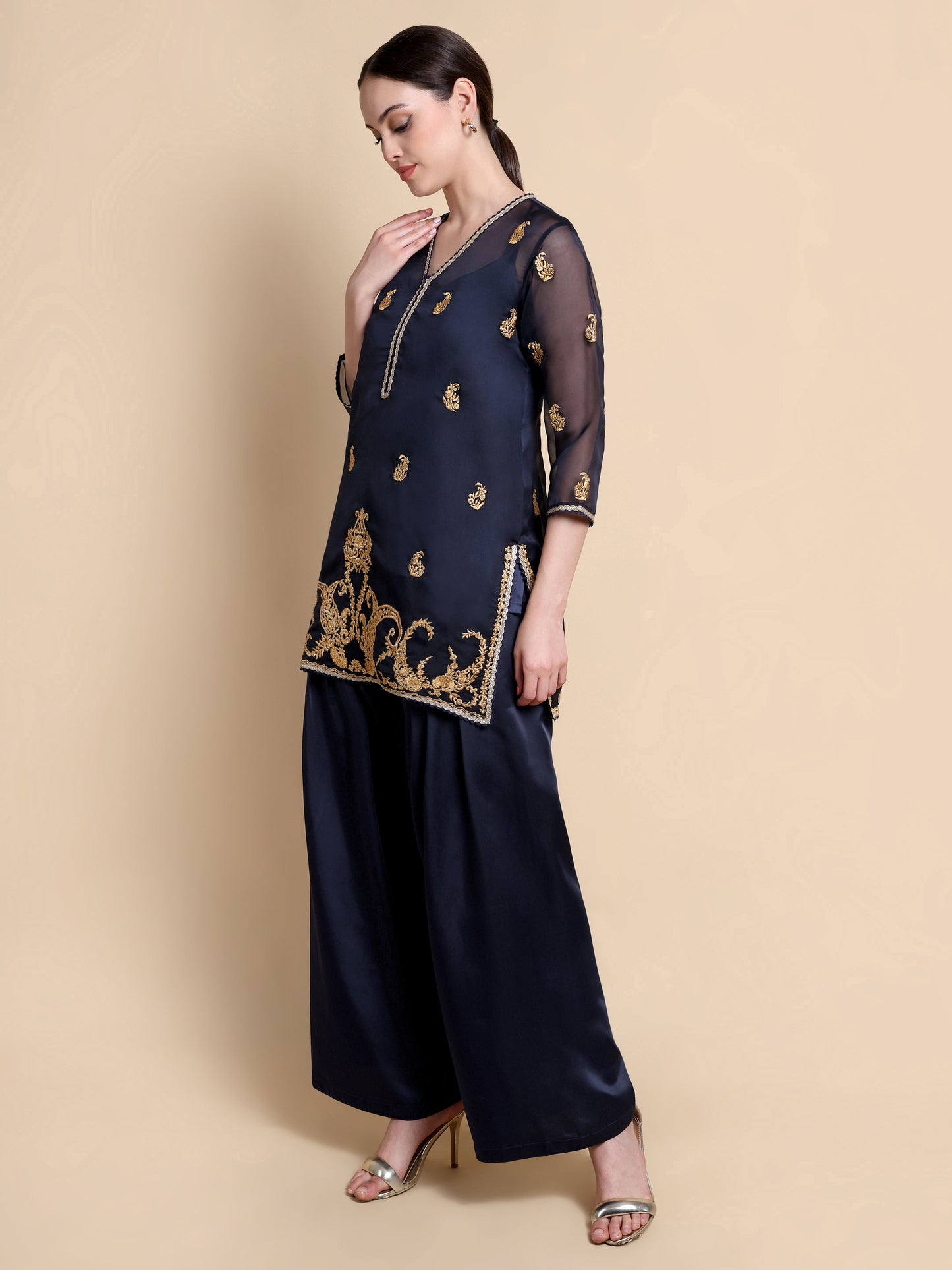 Woman wearing a navy blue traditional outfit with gold embroidery on a beige background