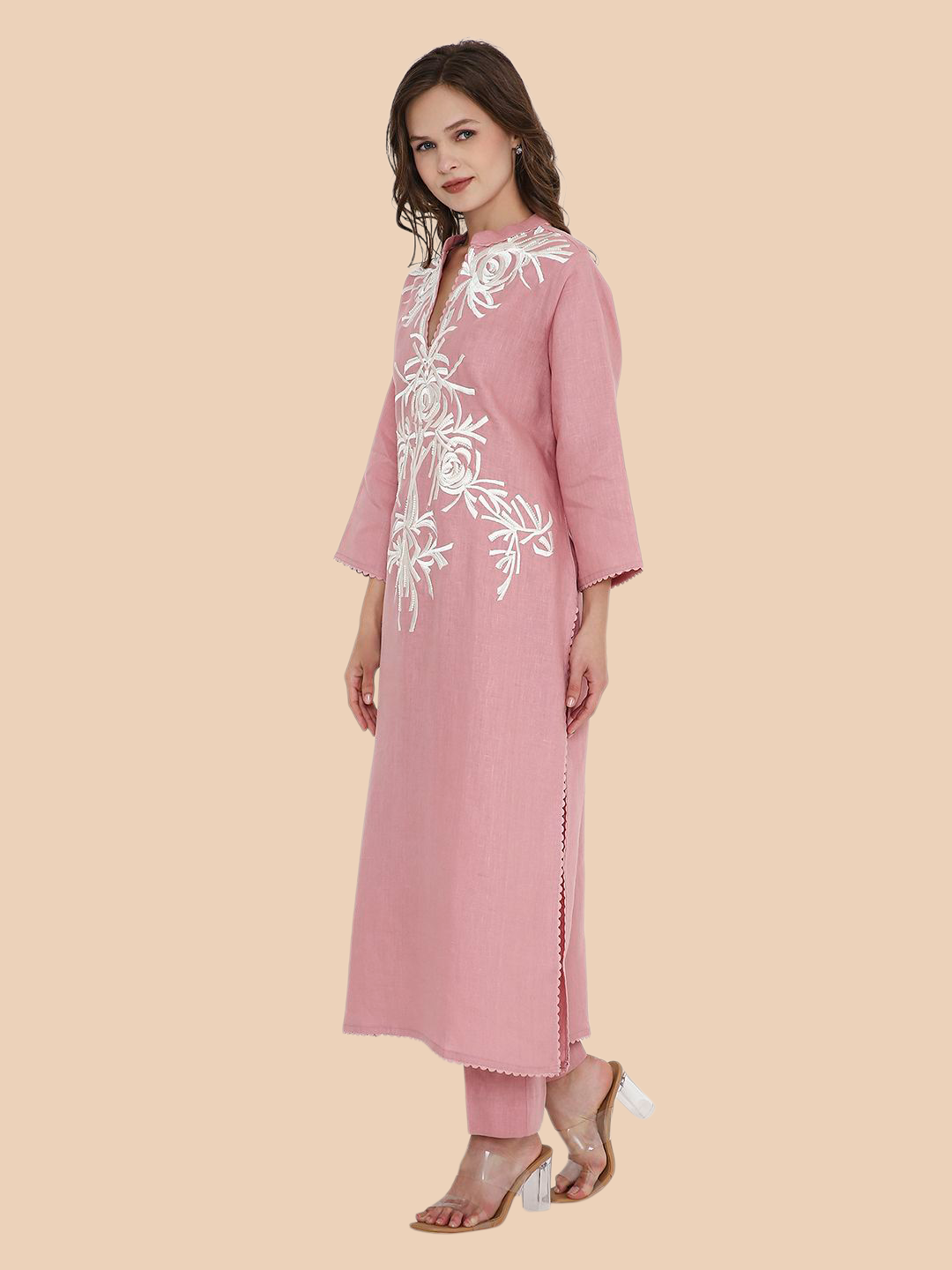 Woman wearing a pink kurta with white floral embroidery on a beige background