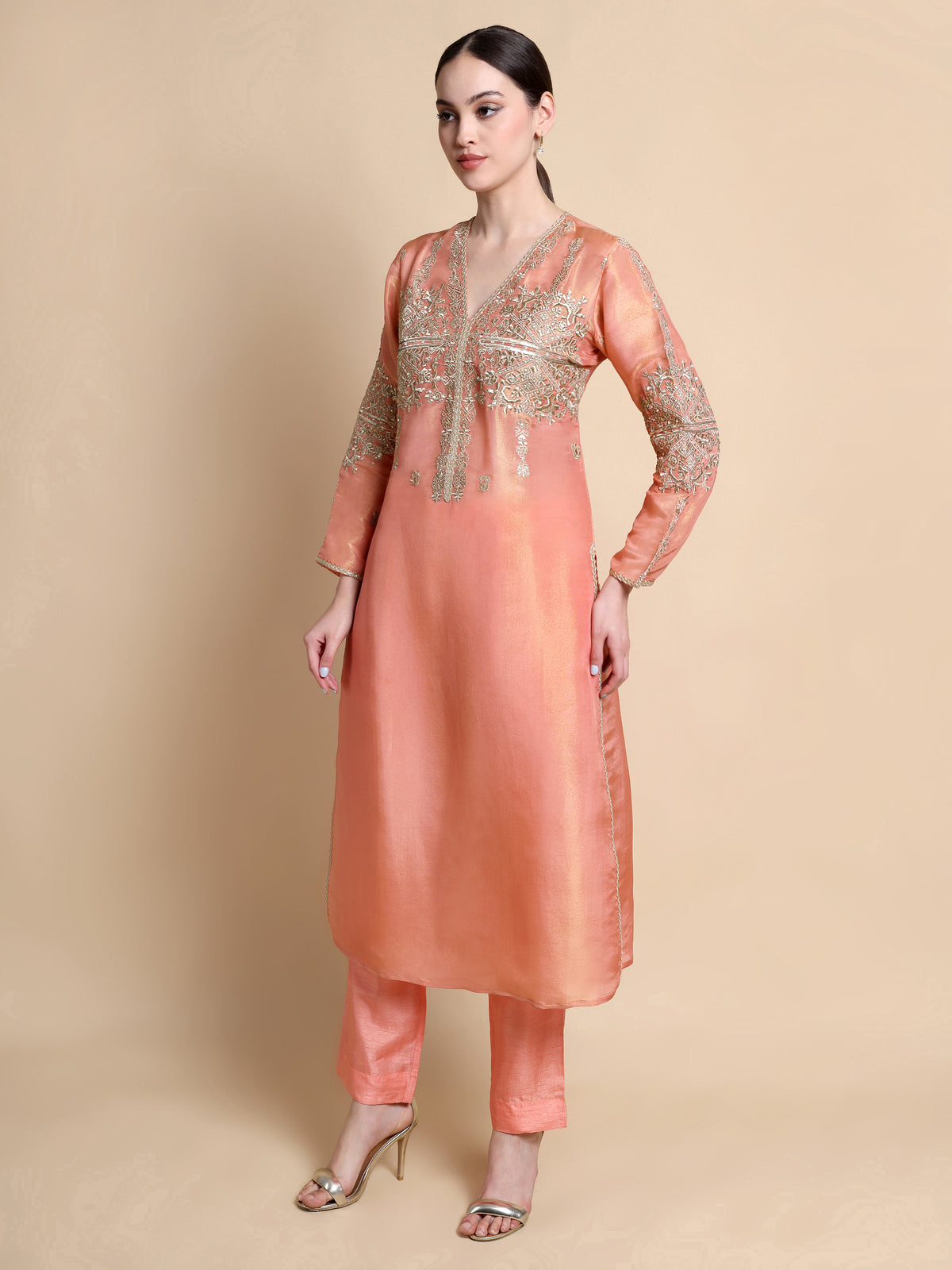 Woman wearing a peach kurta with gold embroidery on a beige background