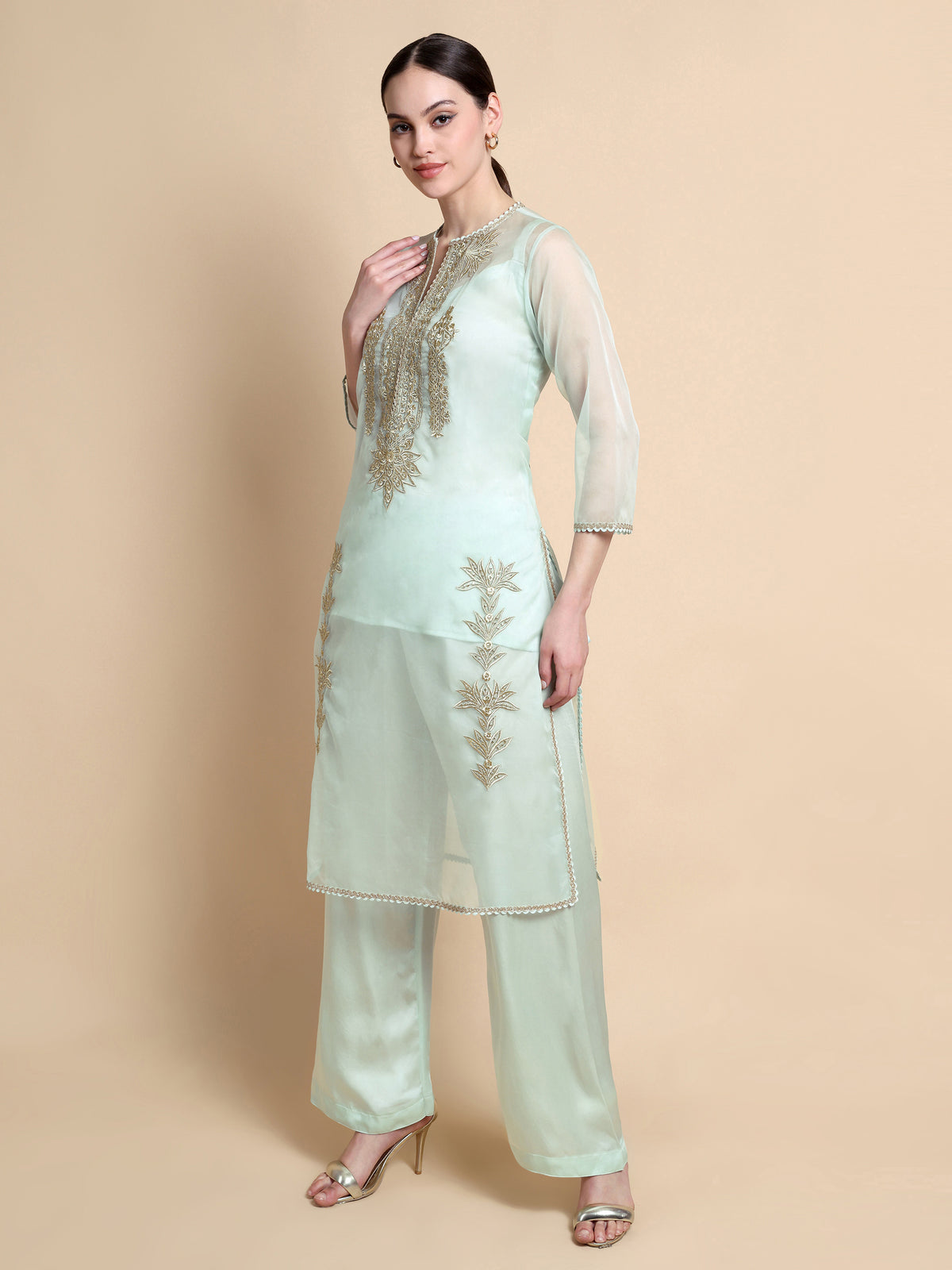 Woman wearing a light green embroidered outfit on a beige background