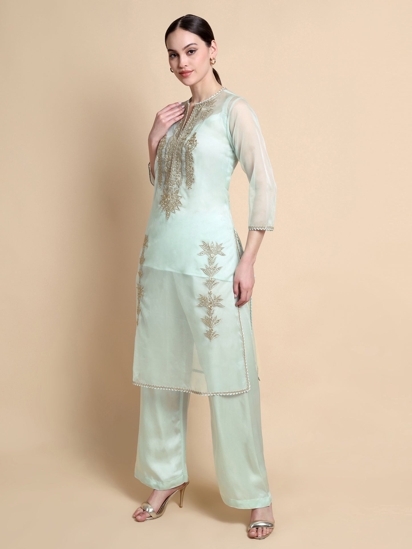 Woman wearing a light green embroidered outfit on a beige background