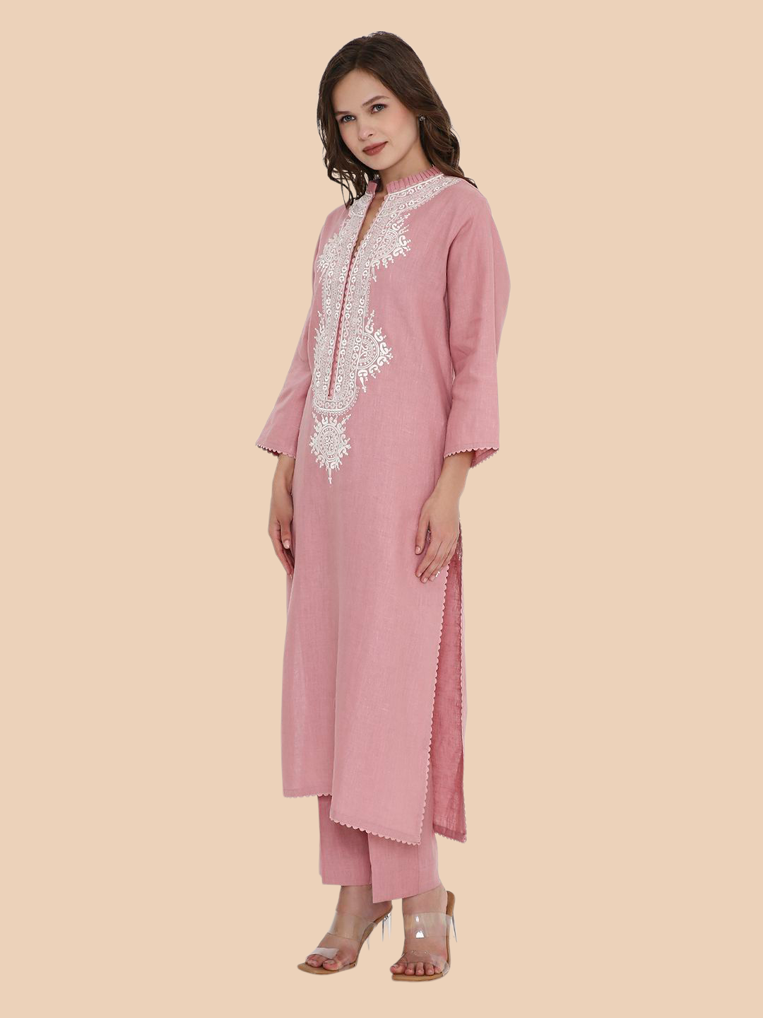 Woman wearing a pink traditional outfit with white embroidery on a beige background