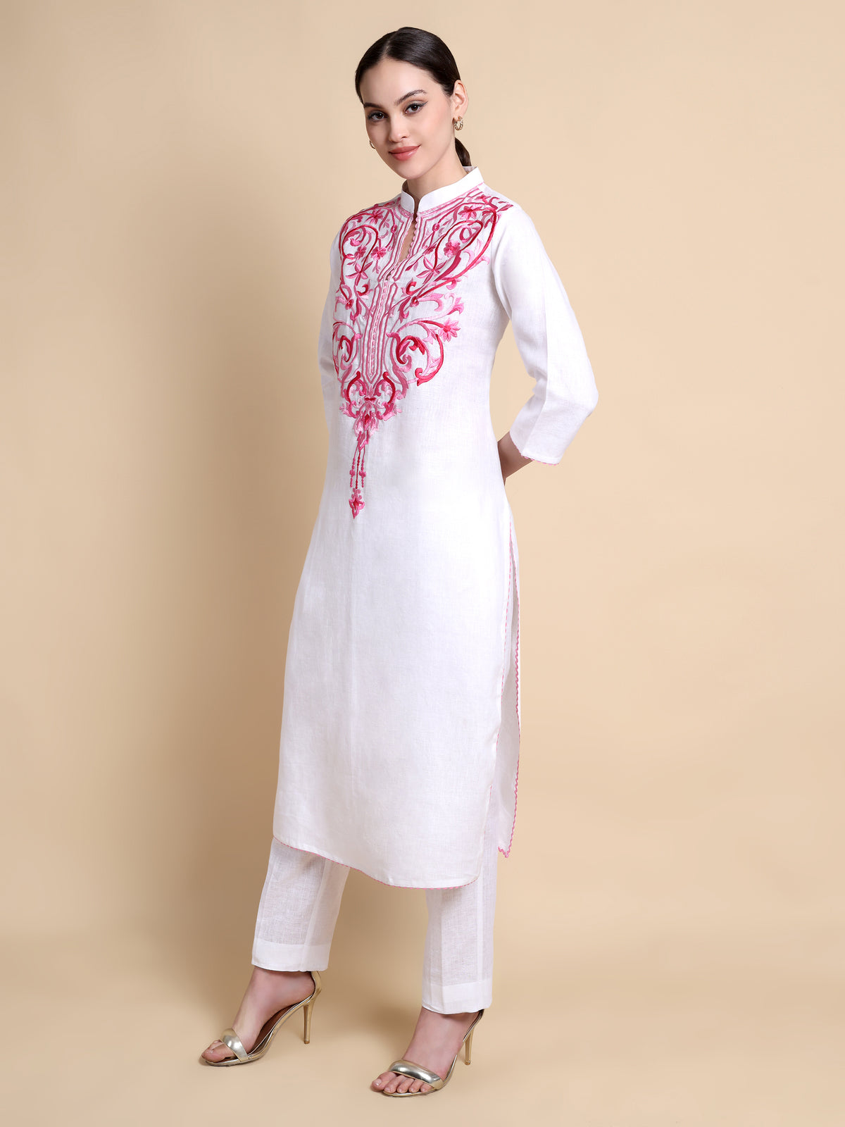 Woman wearing a white kurta with pink embroidery on a beige background