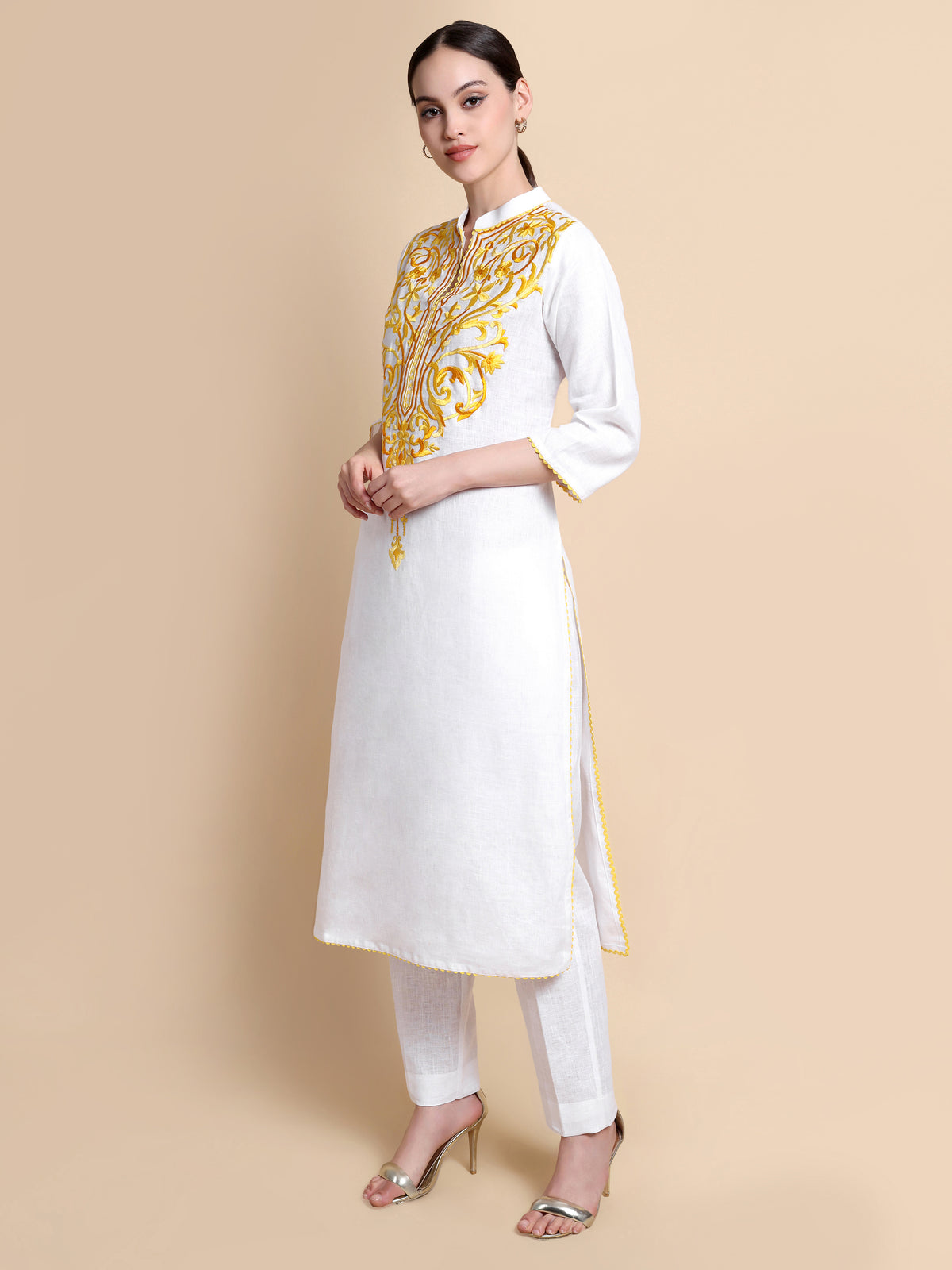 Woman wearing a white kurta with yellow embroidery on a beige background