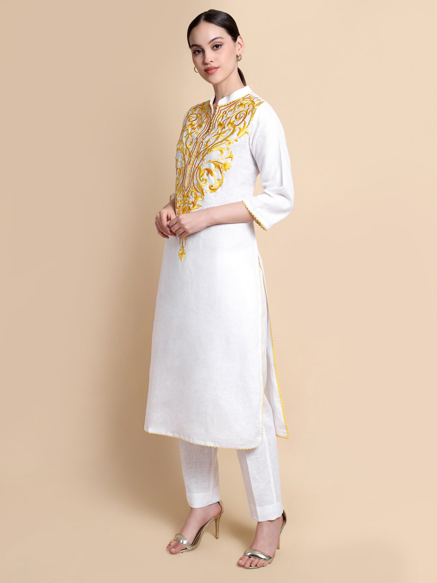 Woman wearing a white kurta with yellow embroidery on a beige background