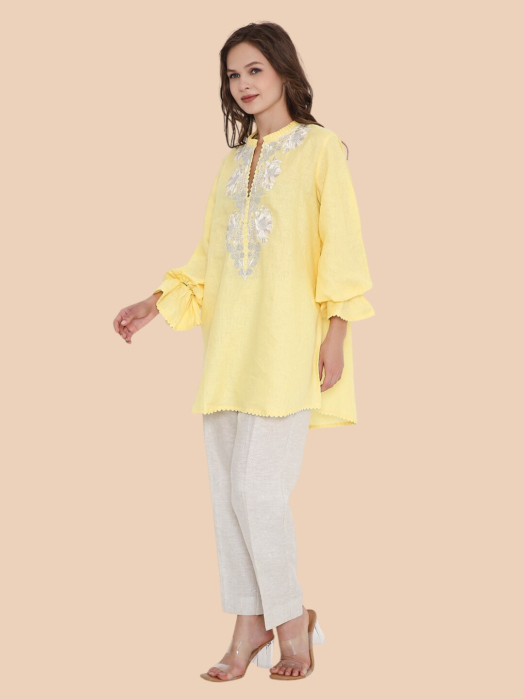 Woman wearing a yellow embroidered top and white pants on a beige background