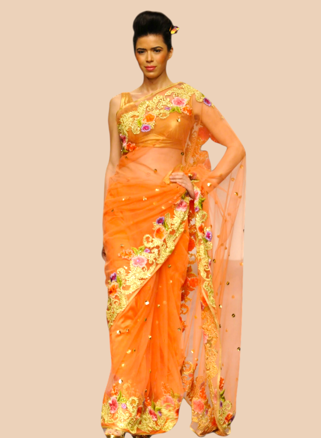 Woman wearing an orange saree with floral patterns on a beige background