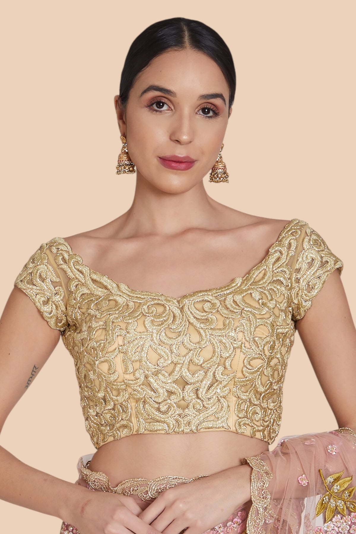 Beautiful pink and gold sari complemented by a nude net blouse showcasing exquisite gold scroll embroidery.