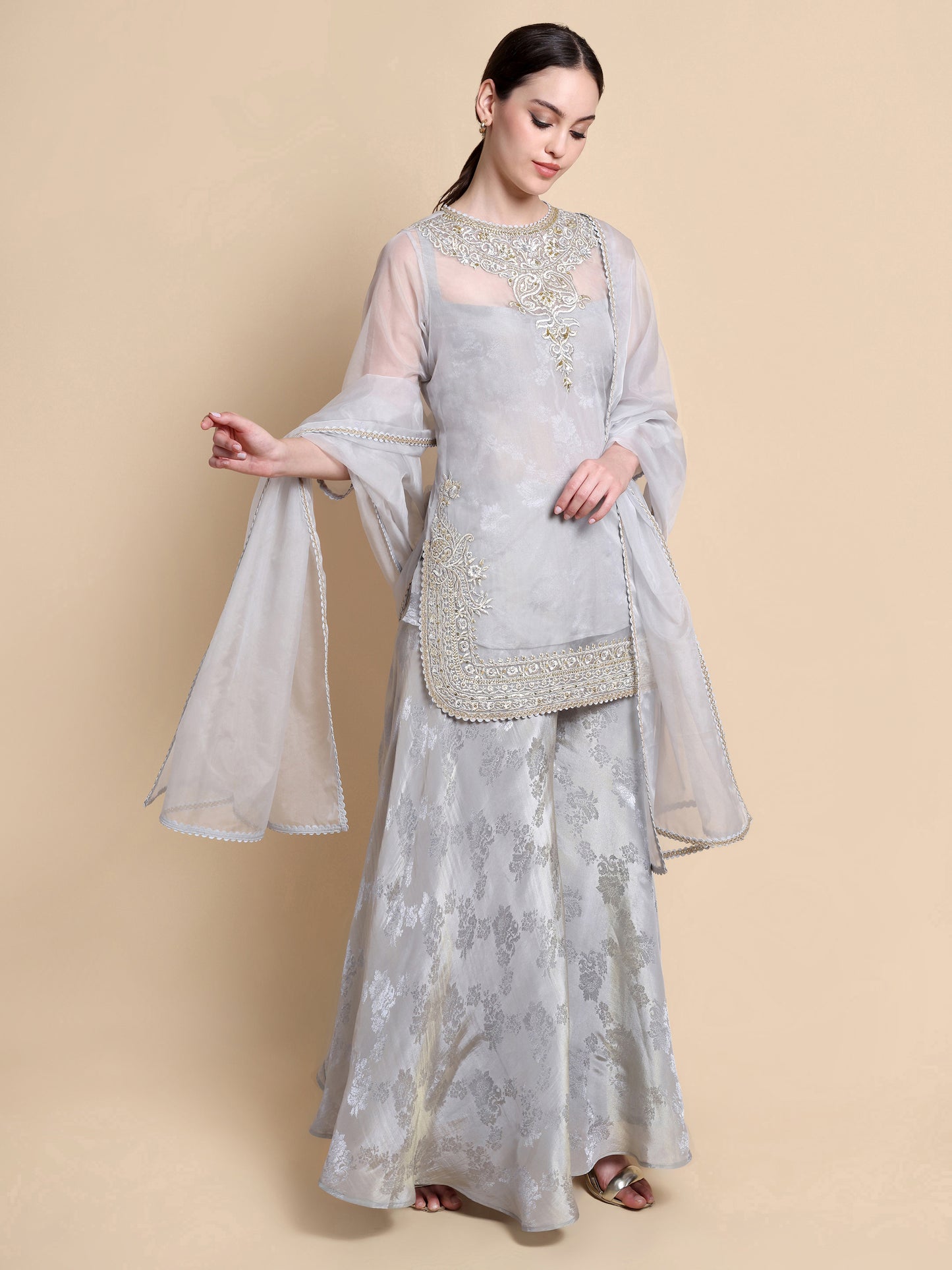 Woman wearing a light gray traditional outfit with floral patterns on a beige background