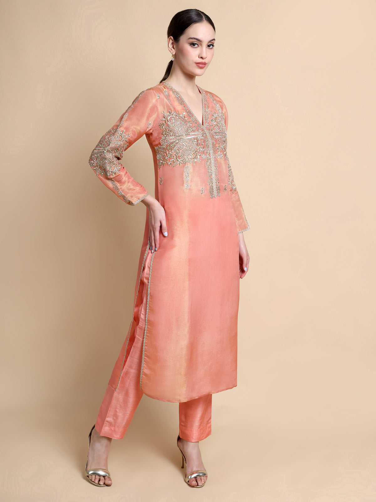 Woman wearing a peach kurta with silver embroidery on a beige background