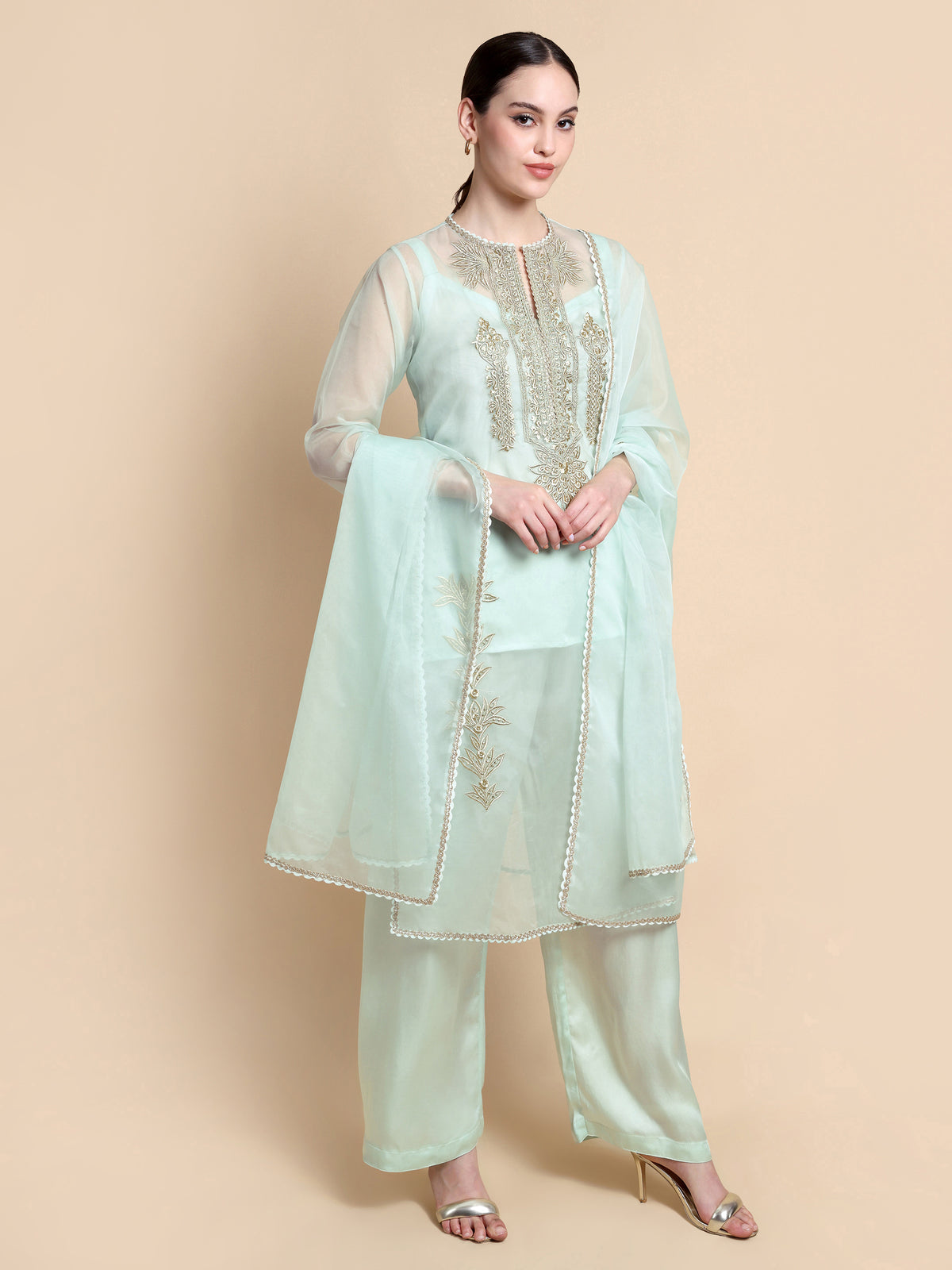 Woman wearing a light blue embroidered outfit on a beige background