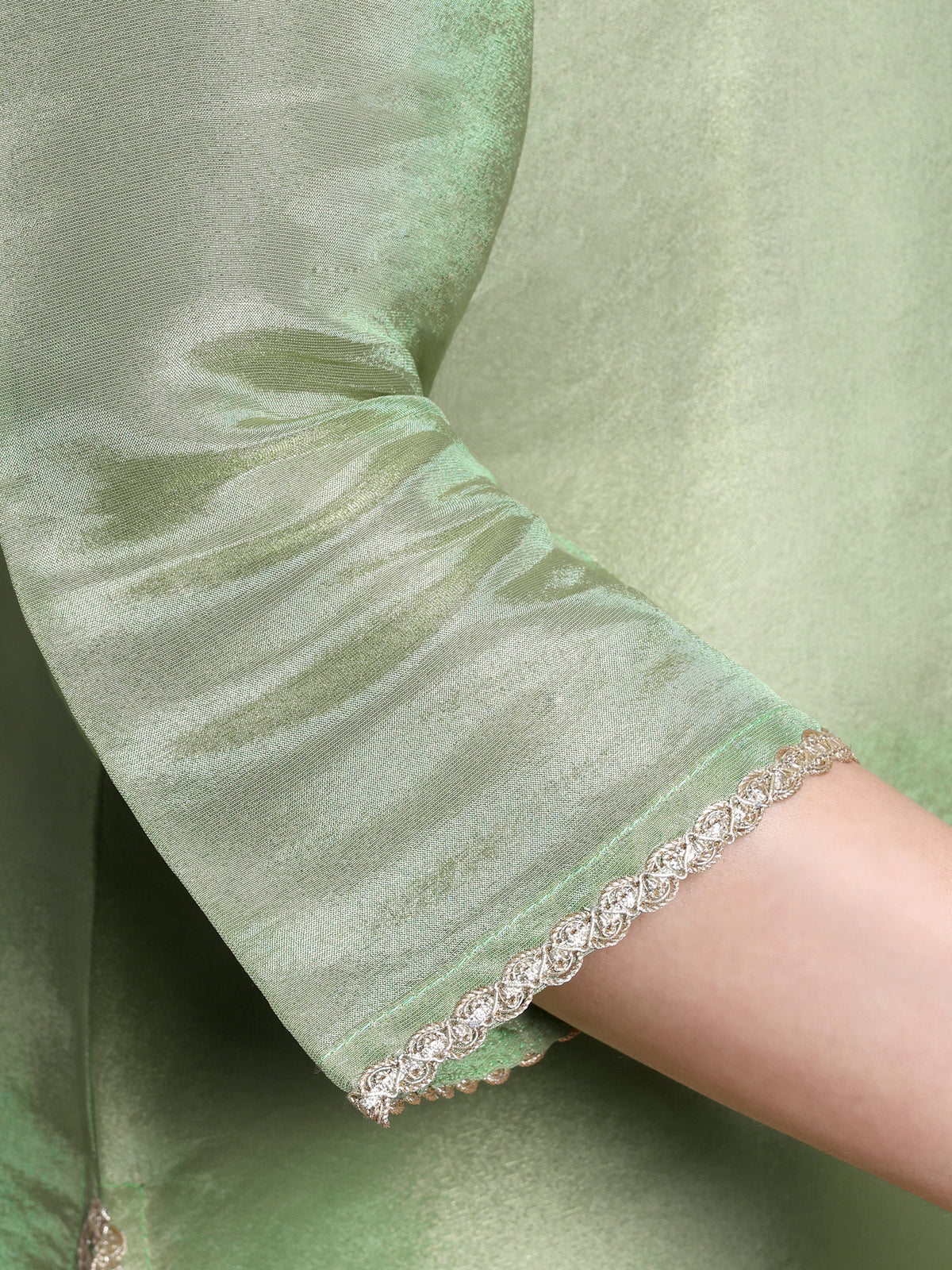 Close-up of a green garment with a decorative hem on a plain background