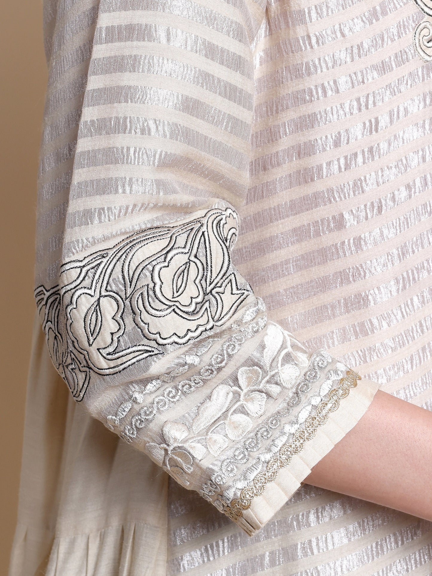 Close-up of a white garment with black floral embroidery on a beige background