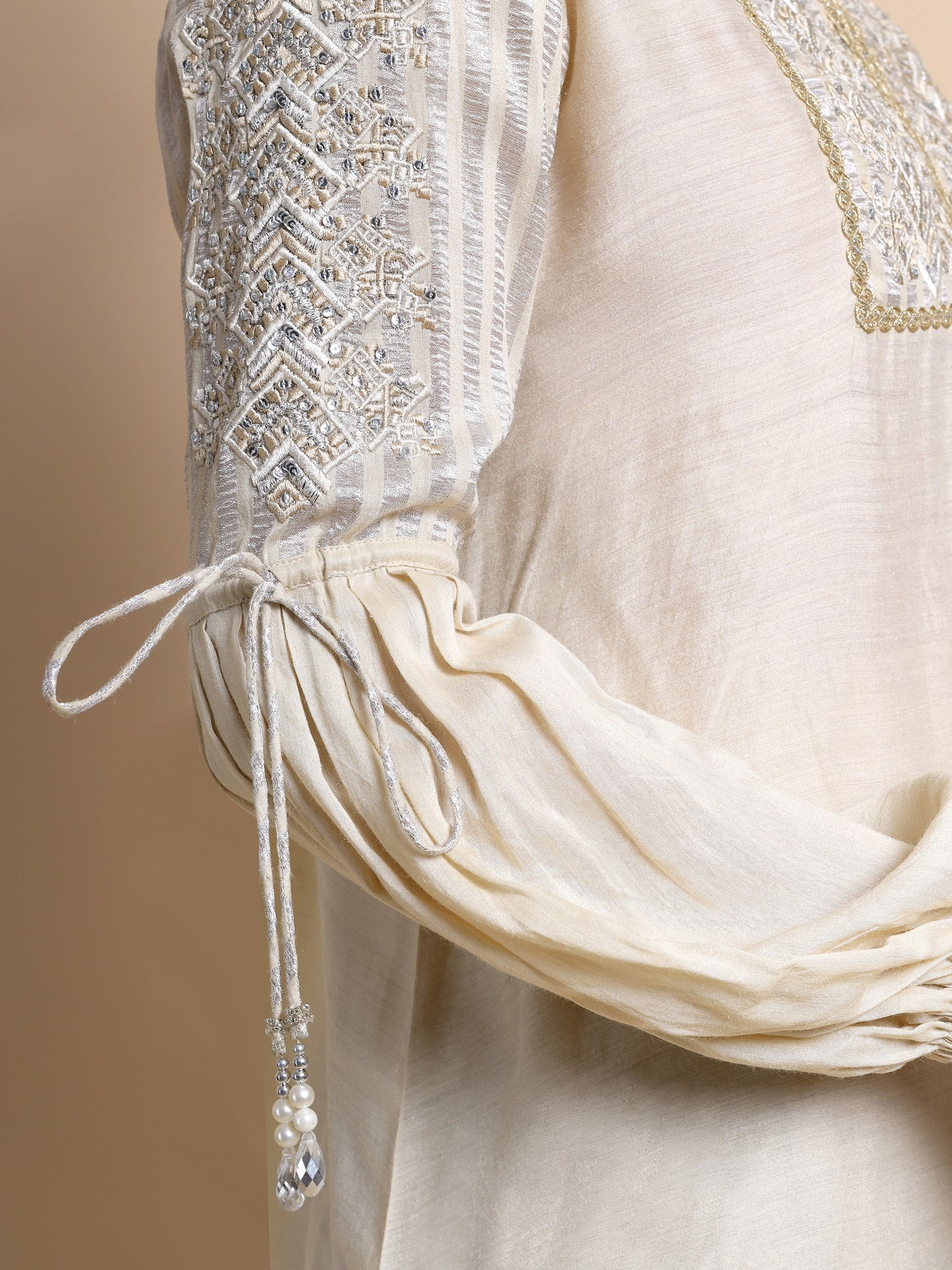 Close-up of a cream-colored garment with intricate beading and embroidery on a beige background