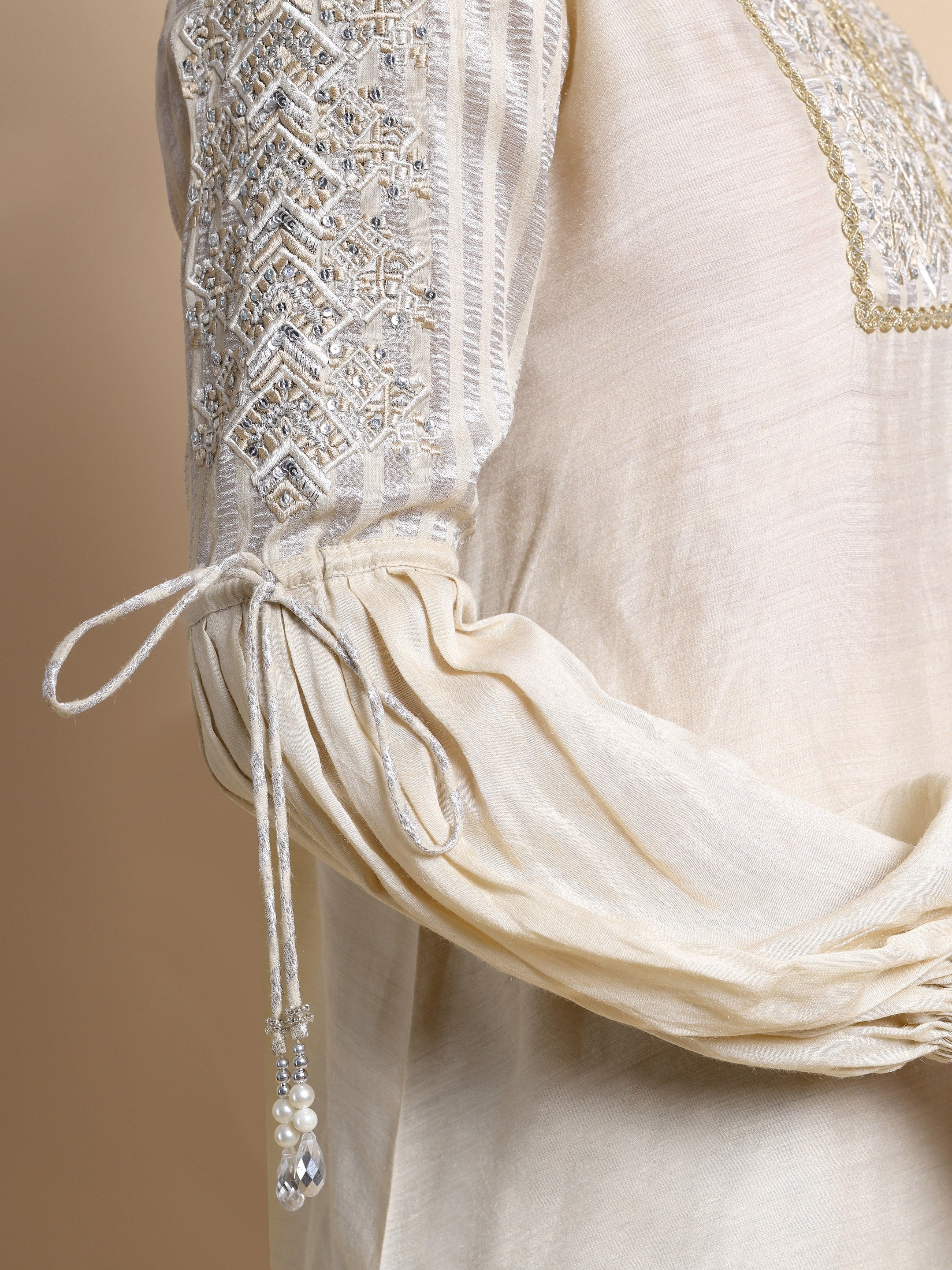 Close-up of a cream-colored garment with intricate beading and embroidery on a beige background