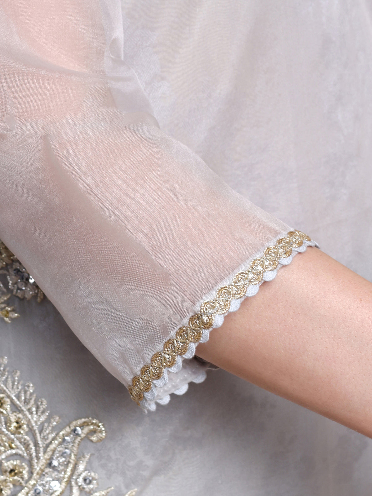 Close-up of a white garment with gold lace trim on a soft gray background