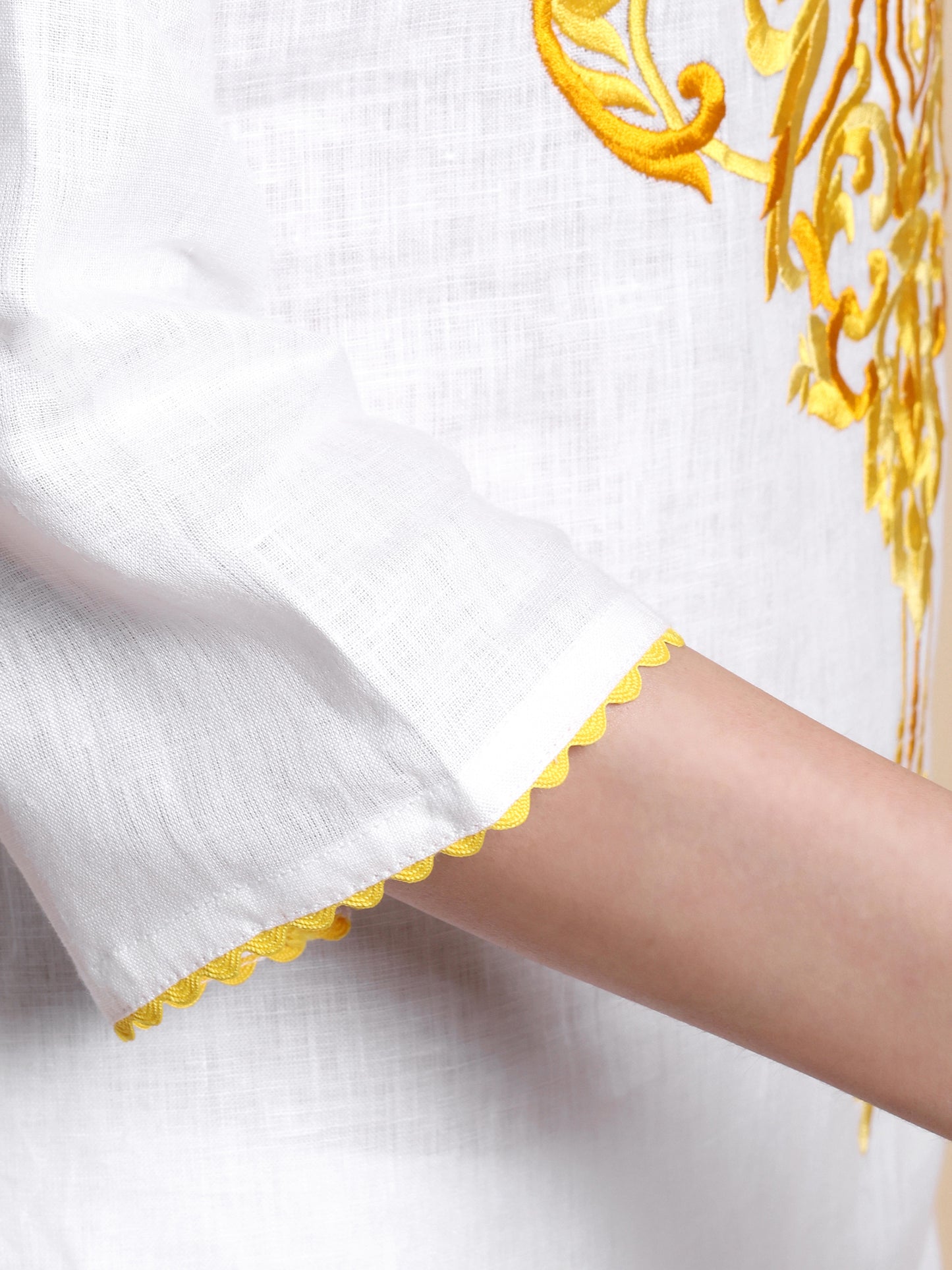 Close-up of a white garment with yellow embroidery on a plain background