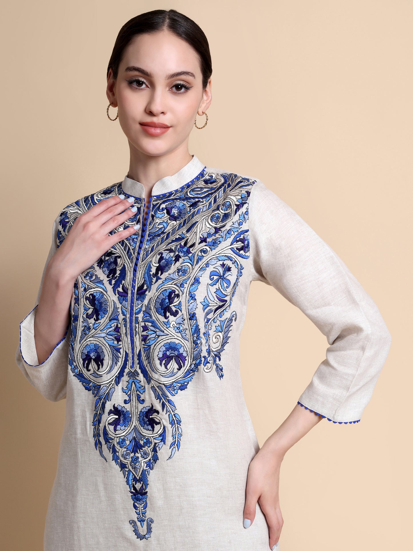 Woman wearing a white kurta with blue and purple floral embroidery on a beige background
