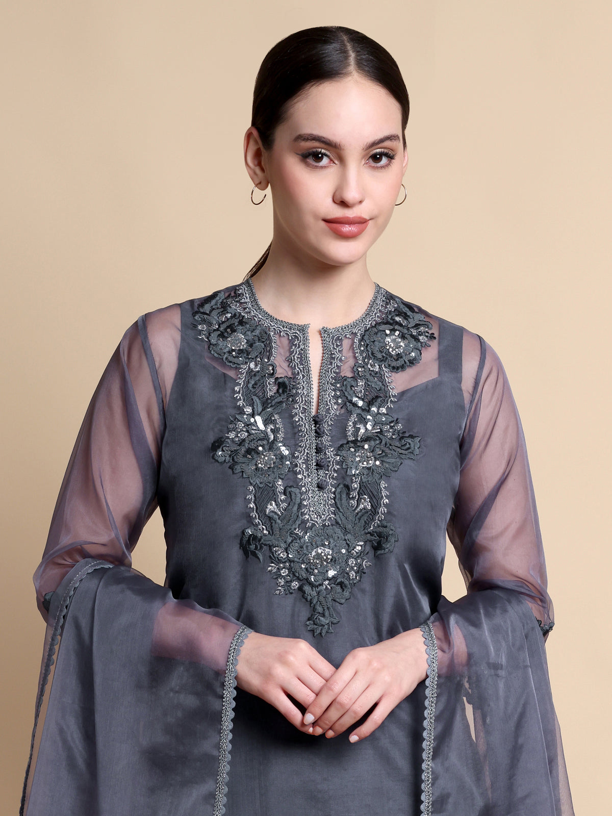 Woman wearing a gray embroidered dress with sheer sleeves on a beige background