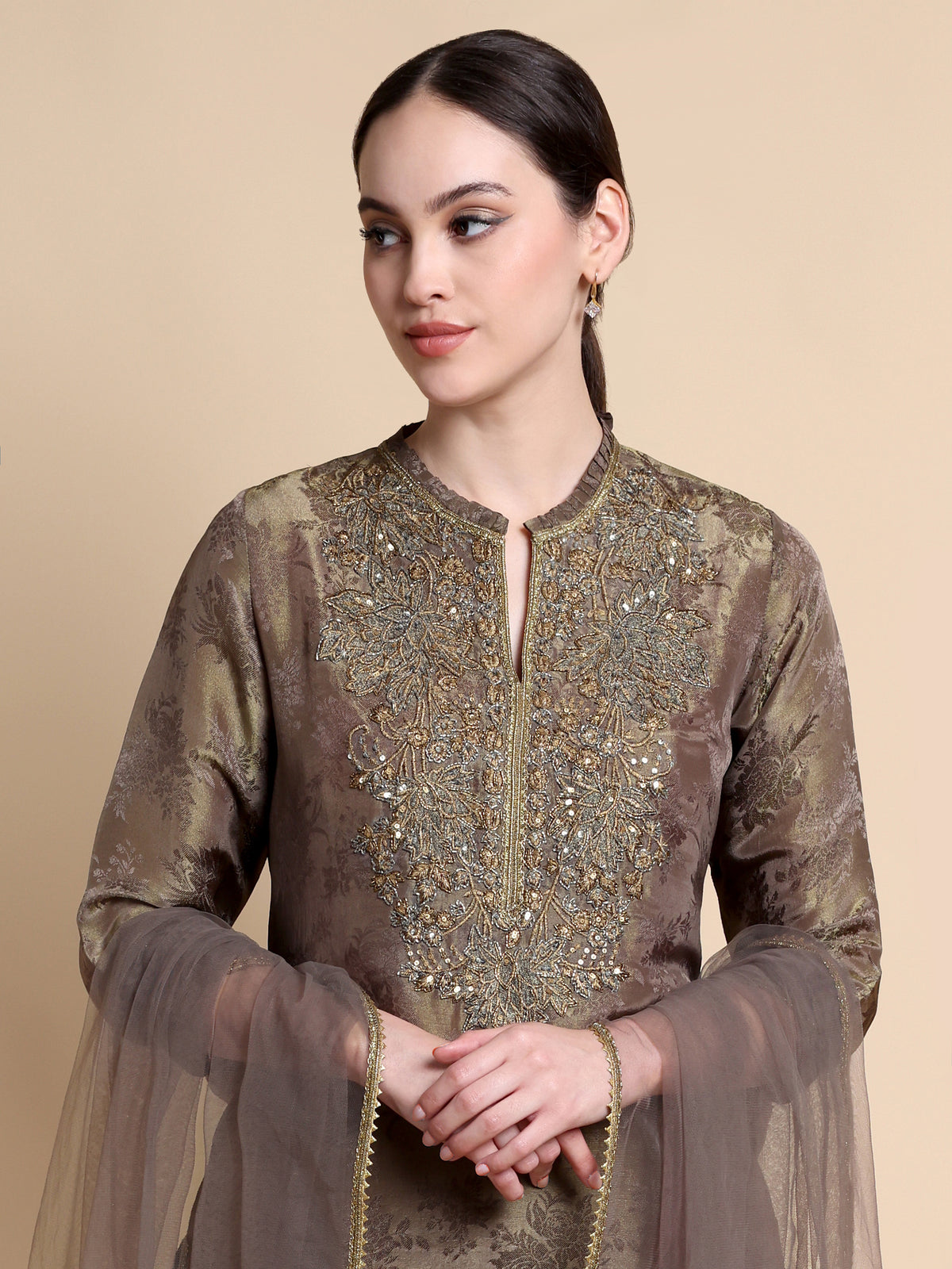 Woman wearing a brown embroidered outfit on a beige background