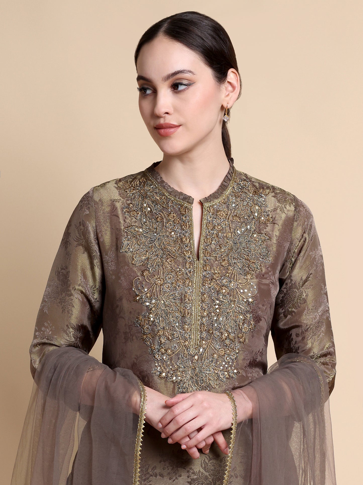 Woman wearing a brown embroidered outfit on a beige background