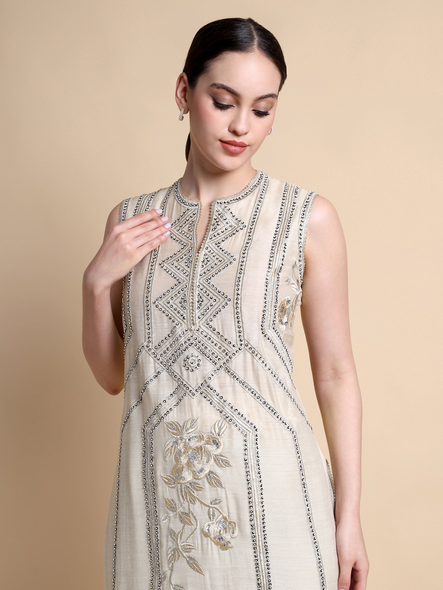 Woman wearing a beige embroidered dress against a beige background