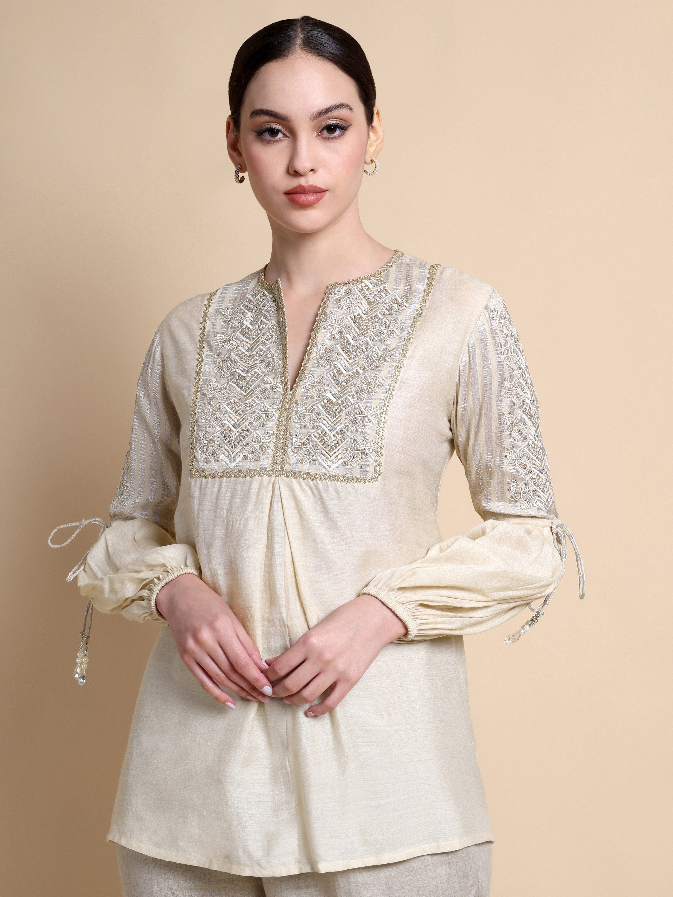 Woman wearing a cream-colored kurta with intricate lace detailing on a beige background