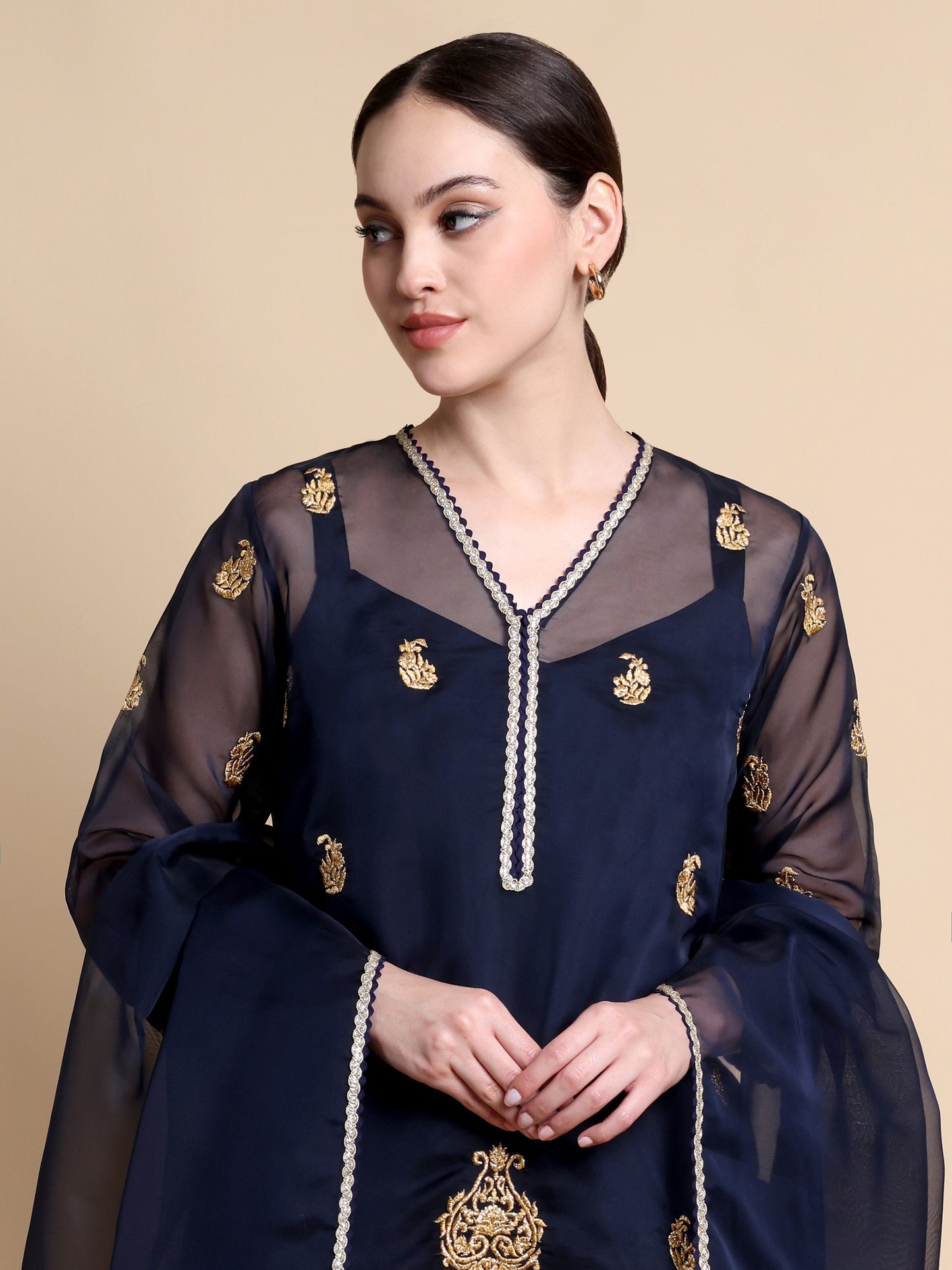 Woman wearing a navy blue traditional outfit with gold embroidery on a beige background