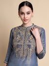 Woman wearing a blue embroidered top against a beige background