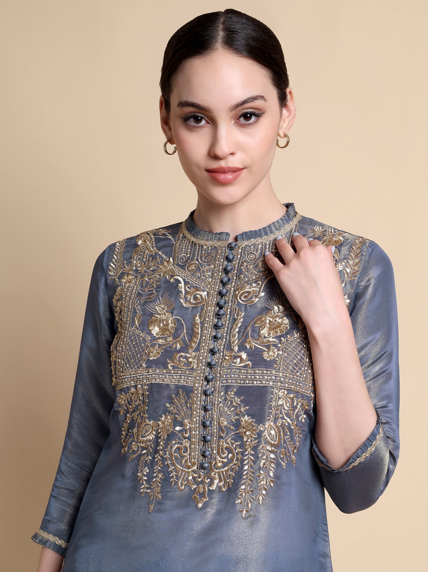 Woman wearing a blue embroidered top against a beige background