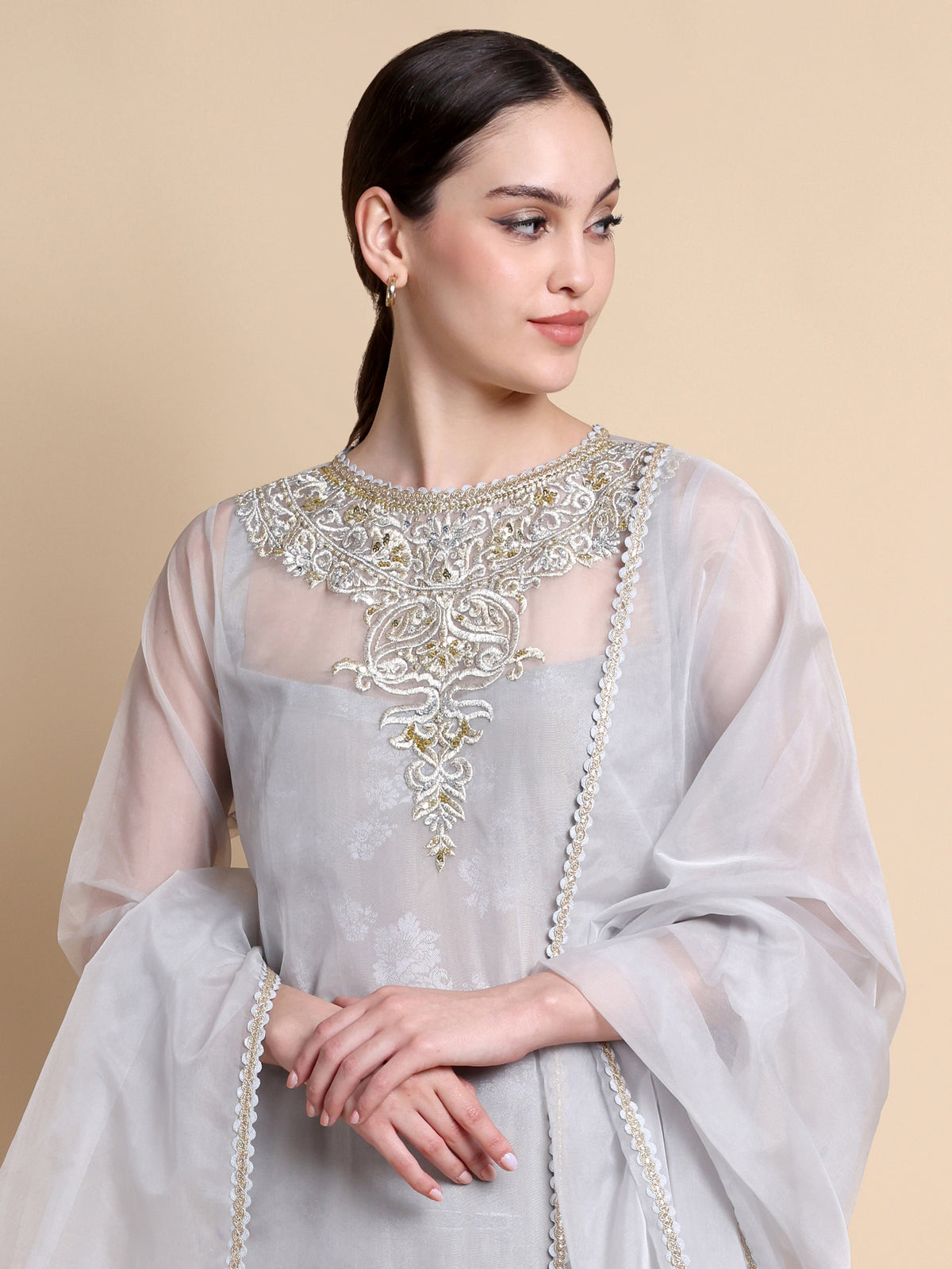 Woman wearing a light gray traditional outfit with intricate embroidery on a beige background