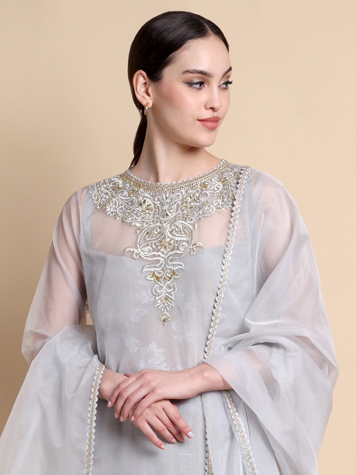 Woman wearing a light gray traditional outfit with intricate embroidery on a beige background