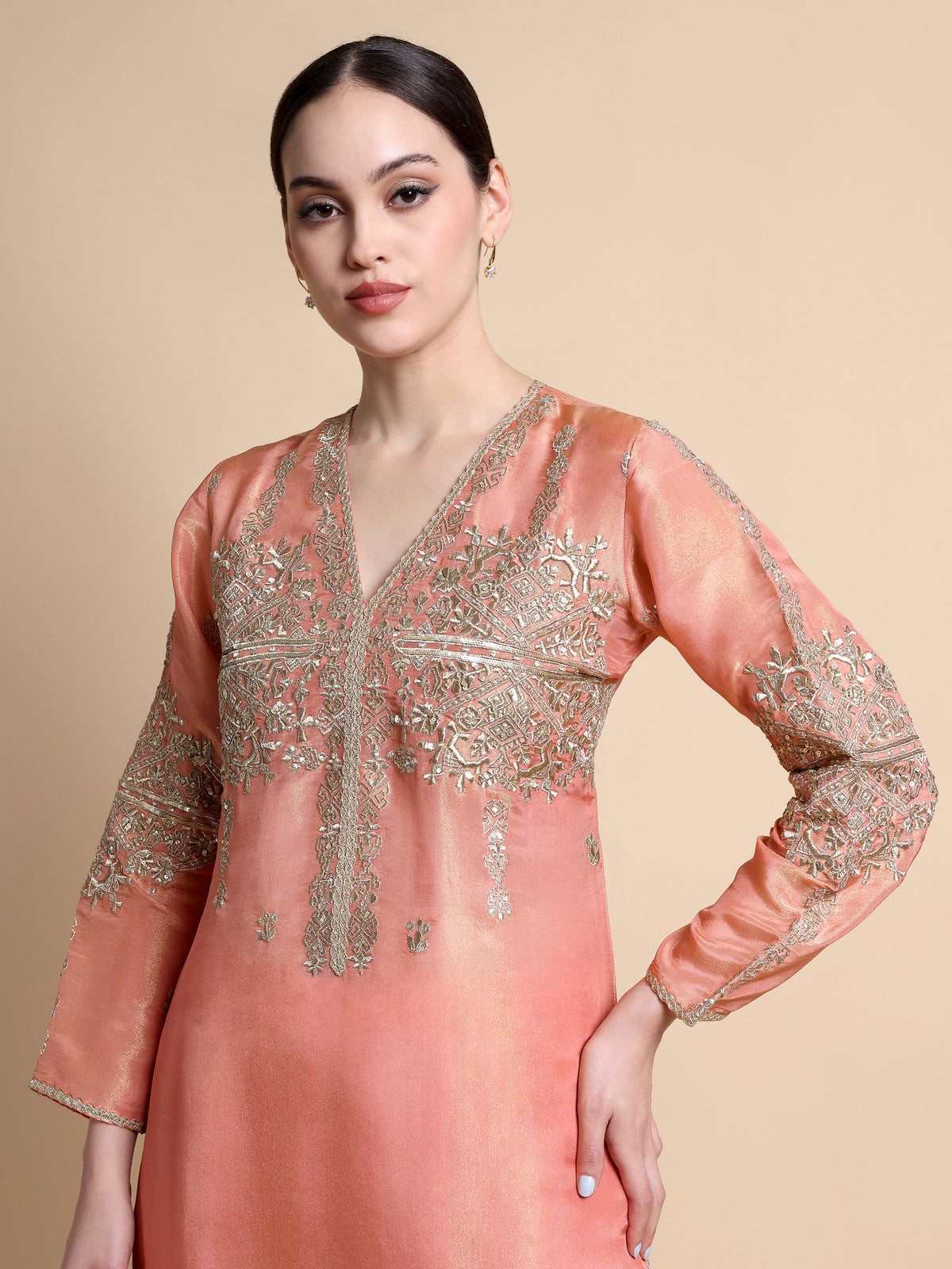 Woman wearing a peach-colored embroidered dress against a beige background