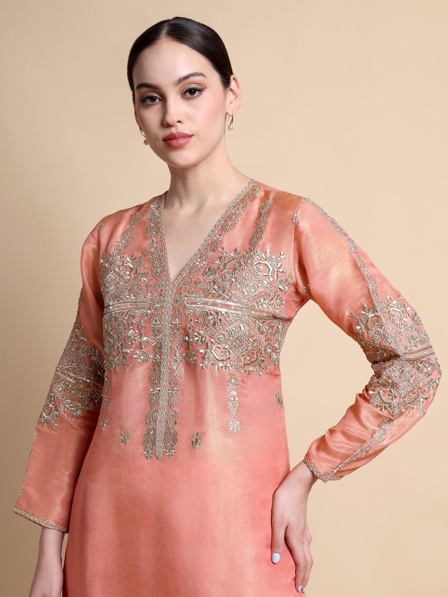 Woman wearing a peach-colored embroidered dress against a beige background