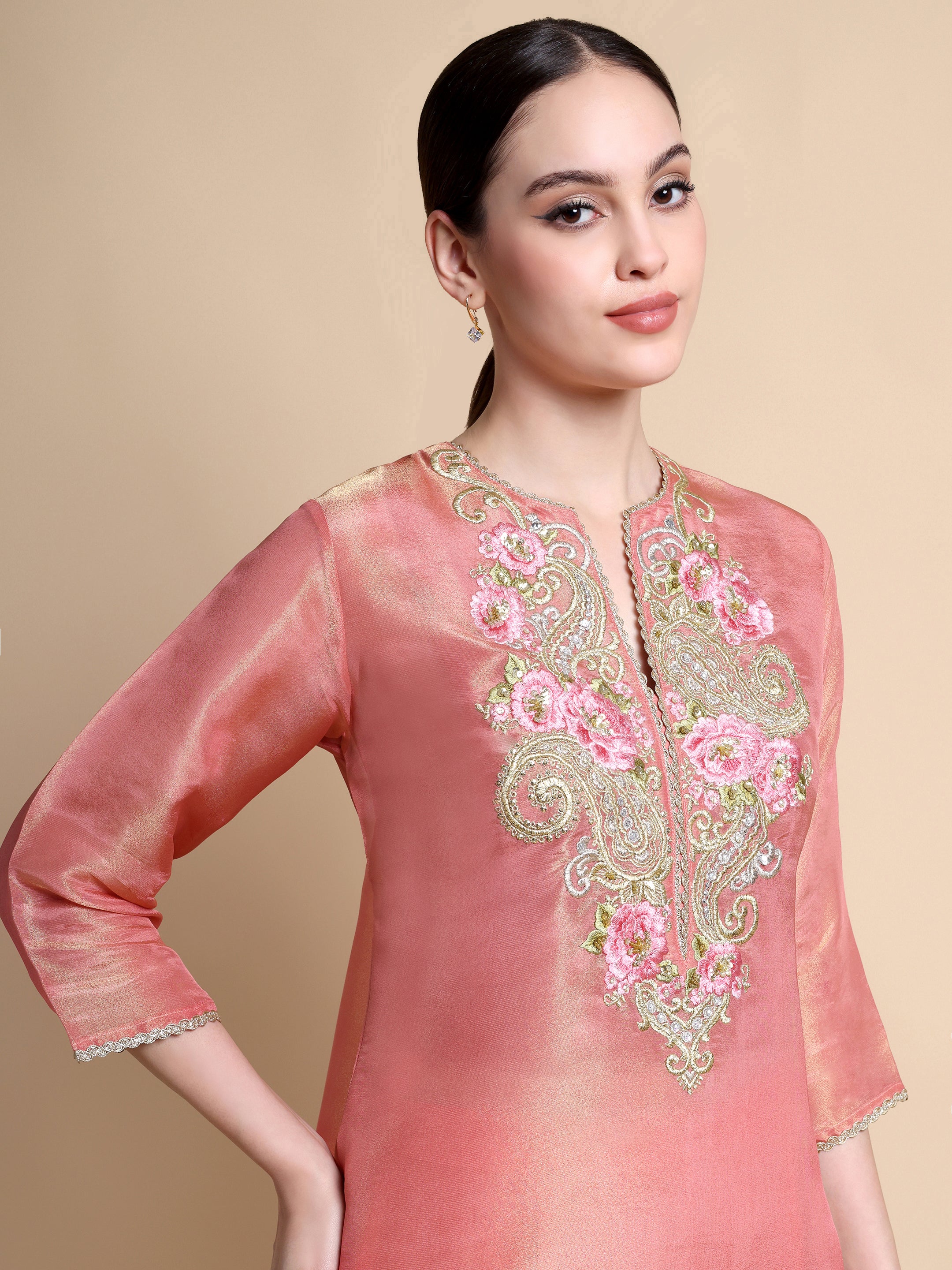 Woman wearing a pink embroidered traditional outfit on a beige background
