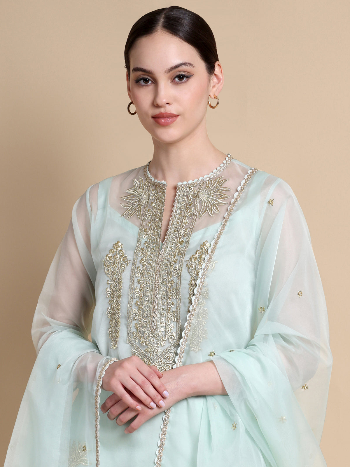 Woman wearing a light blue embroidered traditional outfit on a beige background