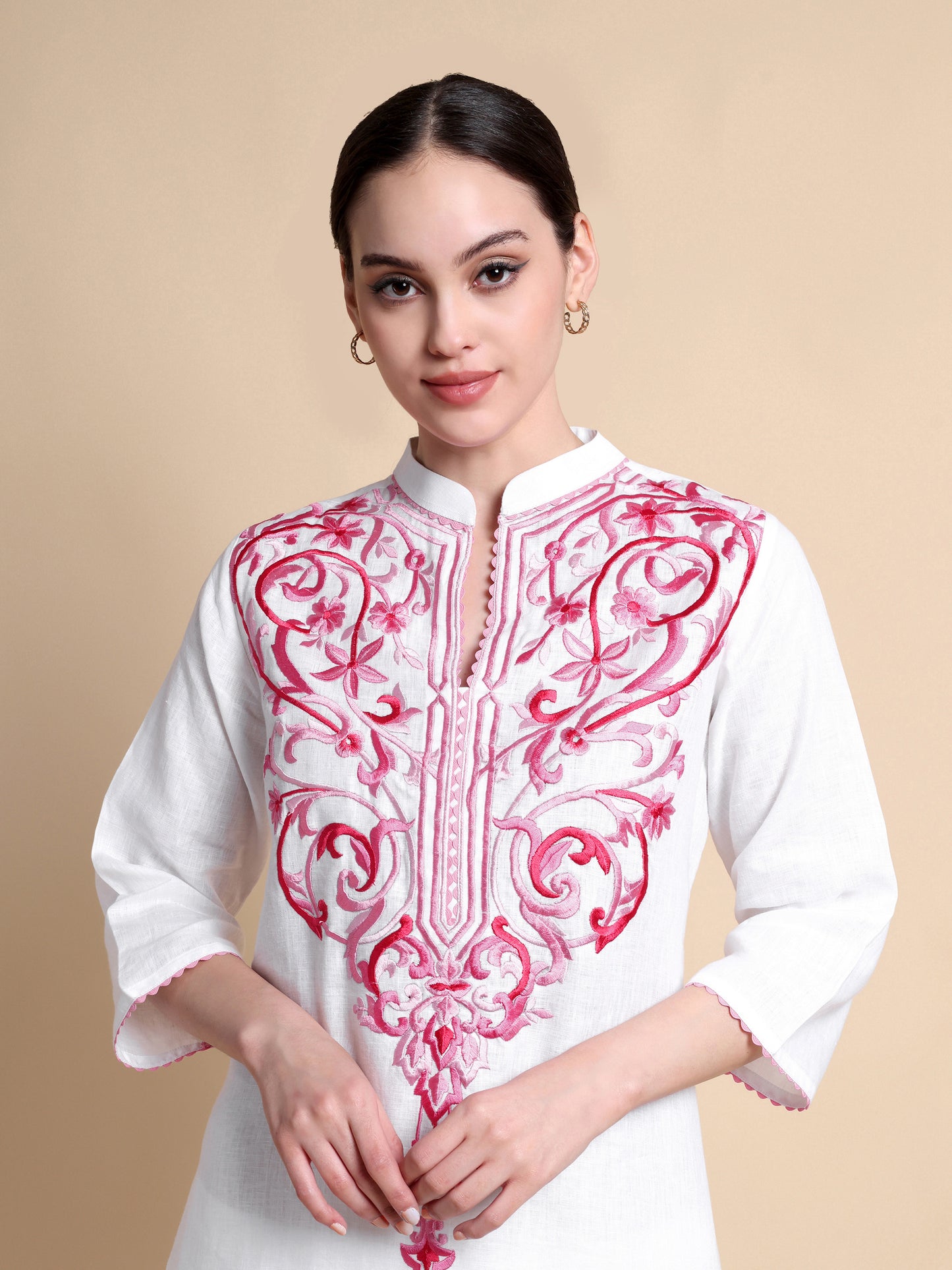 Woman wearing a white kurta with pink embroidery on a beige background