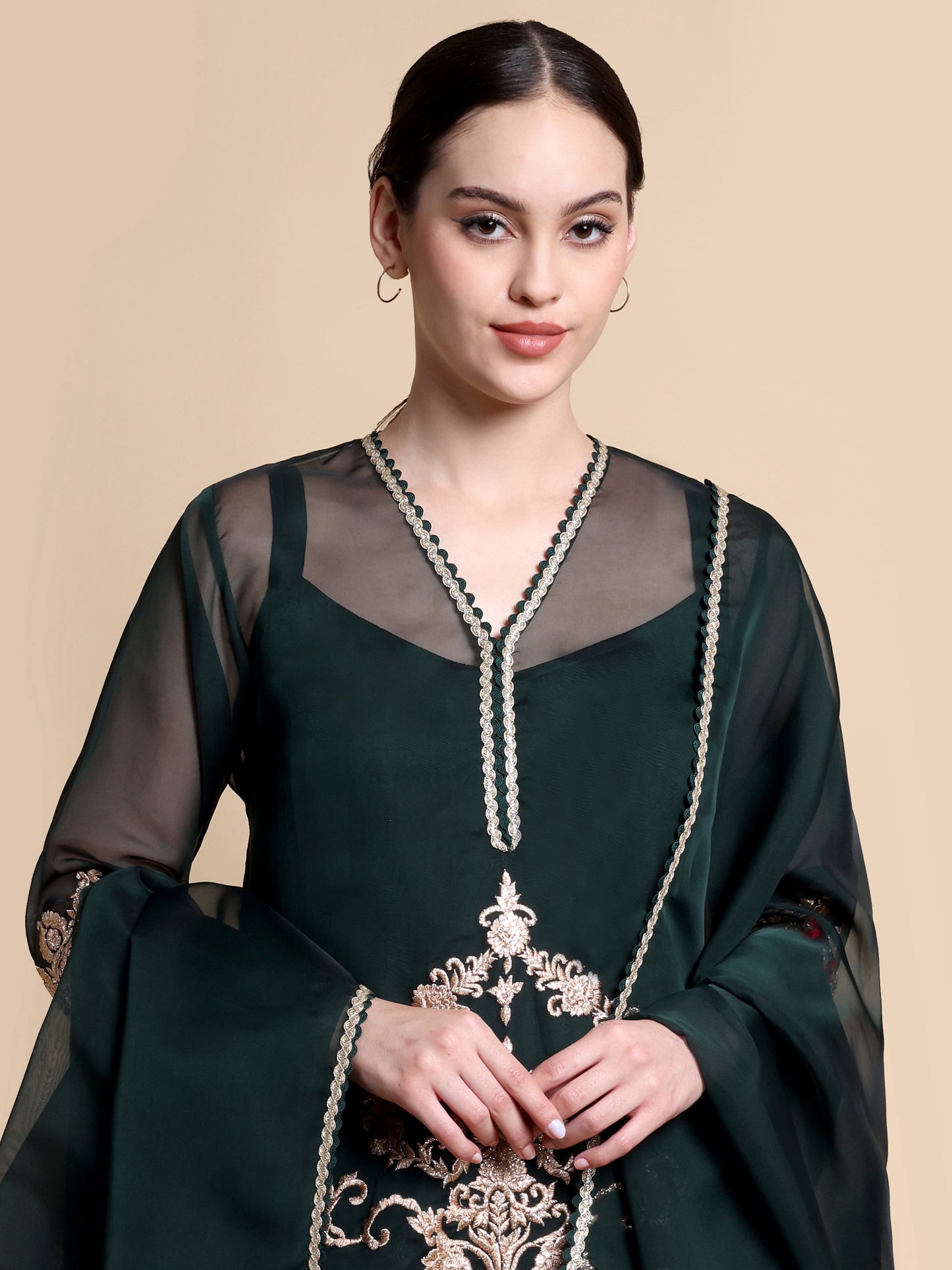 Woman wearing a dark green traditional outfit with intricate embroidery on a beige background